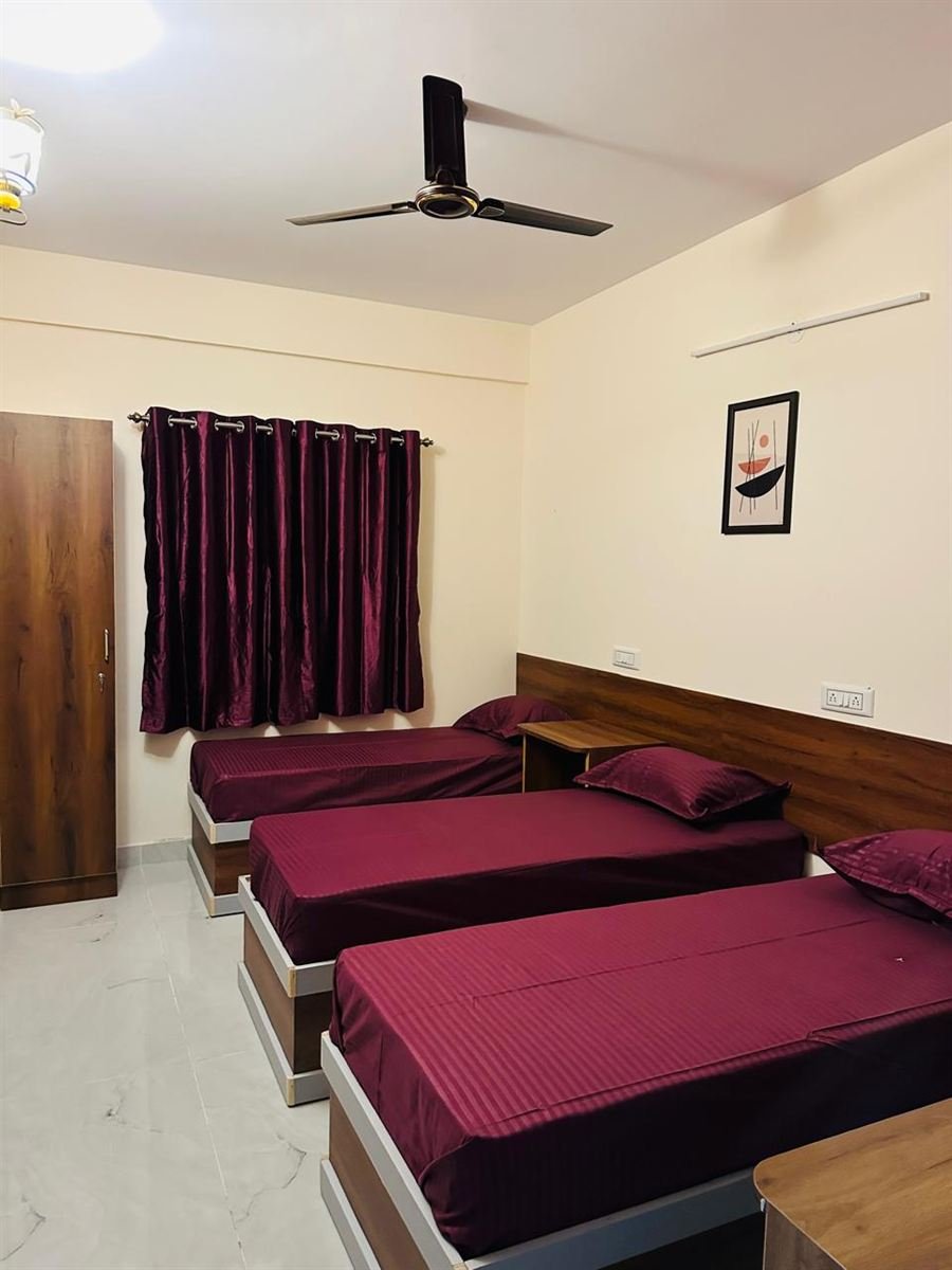 Room at AMIGO Luxury, Marathahalli — triple sharing with maroon bedding and wardrobe